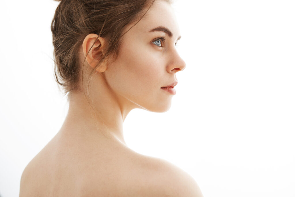 portrait of young beautiful tender nude girl with bun standing back to camera over white background.